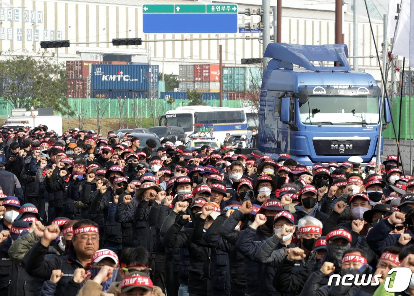 24일 울산 남구 울산신항 앞에서 민주노총 전국공공운수노동조합 화물연대 울산본부 총파업 출정식이 열린 가운데 구호를 외치는 조합원들 뒤로 화물차가 지나가고 있다. 화물연대는 △안전운임 일몰제 폐지 △안전운임제 전차종, 전품목으로 확대 △노동기본권 확대·화물노동자 권리보장 등을 요구하고 있다. 2022.11.24/뉴스1 ⓒ News1 윤일지 기자