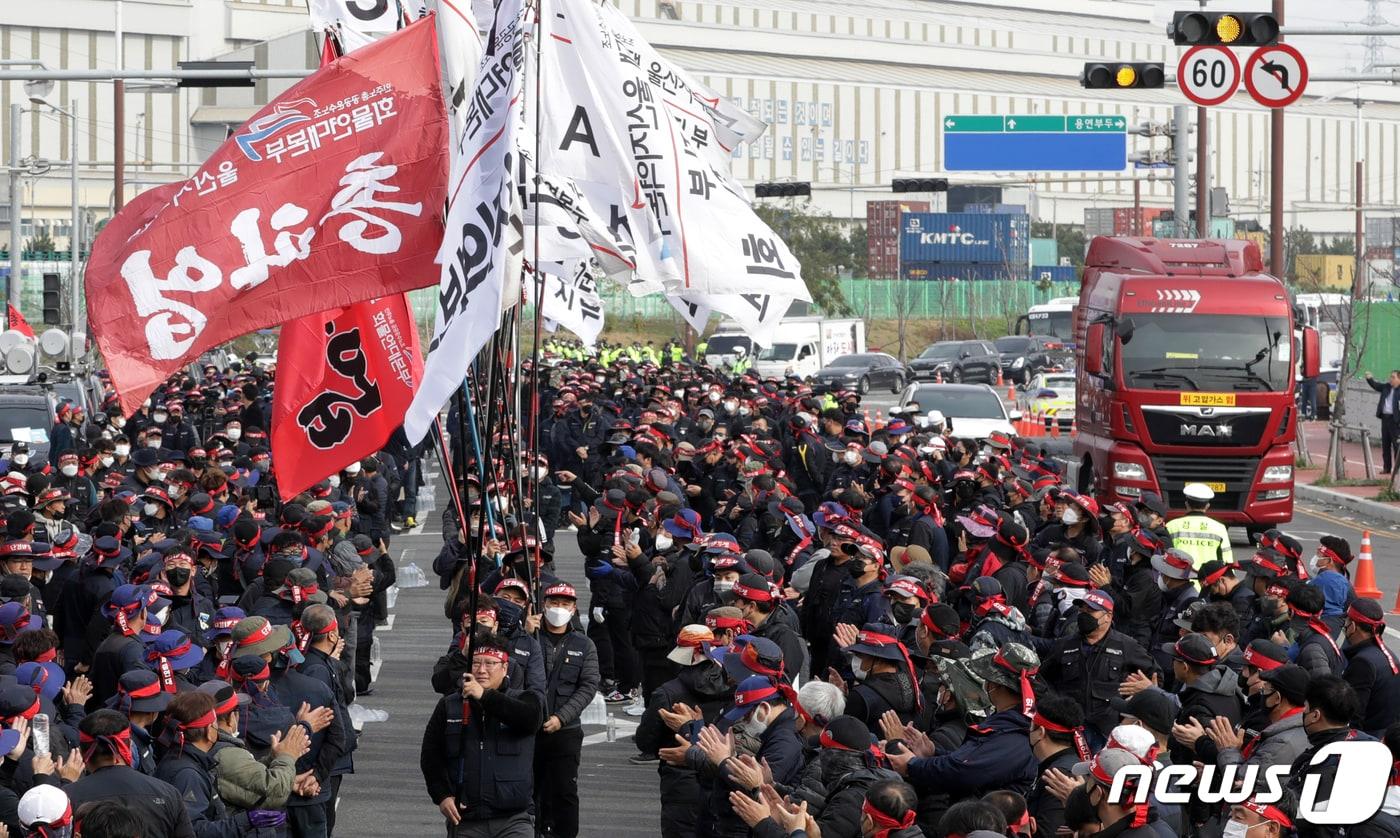 24일 울산 남구 울산신항 앞에서 민주노총 전국공공운수노동조합 화물연대 울산본부 총파업 출정식이 열린 가운데 입장하는 깃발 뒤로 화물차가 지나가고 있다. 화물연대는 △안전운임 일몰제 폐지 △안전운임제 전차종, 전품목으로 확대 △노동기본권 확대·화물노동자 권리보장 등을 요구하고 있다. 2022.11.24/뉴스1 ⓒ News1 윤일지 기자