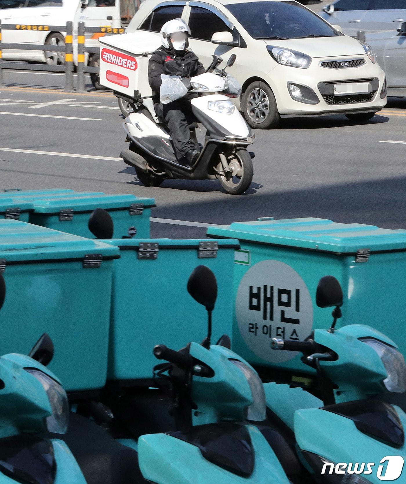 서울 강남구 배민라이더스 남부센터에 서있는 배달용 오토바이 뒤로 배달노동자가 지나가 고 있다.  ⓒ News1 박세연 기자