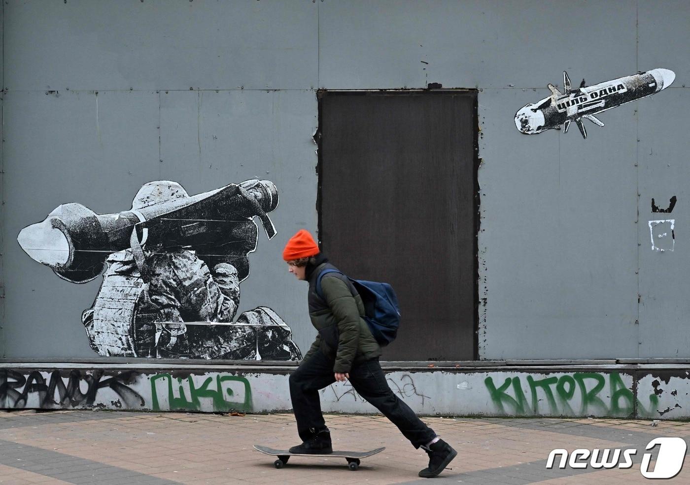 25일&#40;현지시간&#41; 러시아 침공 속 우크라이나 키이우에서 병사가 휴대용 대전차 미사일을 발사하는 모습을 그린 벽화 앞에 소년에 스케이트 보드를 타고 있다. &lt;자료사진&gt; ⓒ AFP=뉴스1 ⓒ News1 우동명 기자
