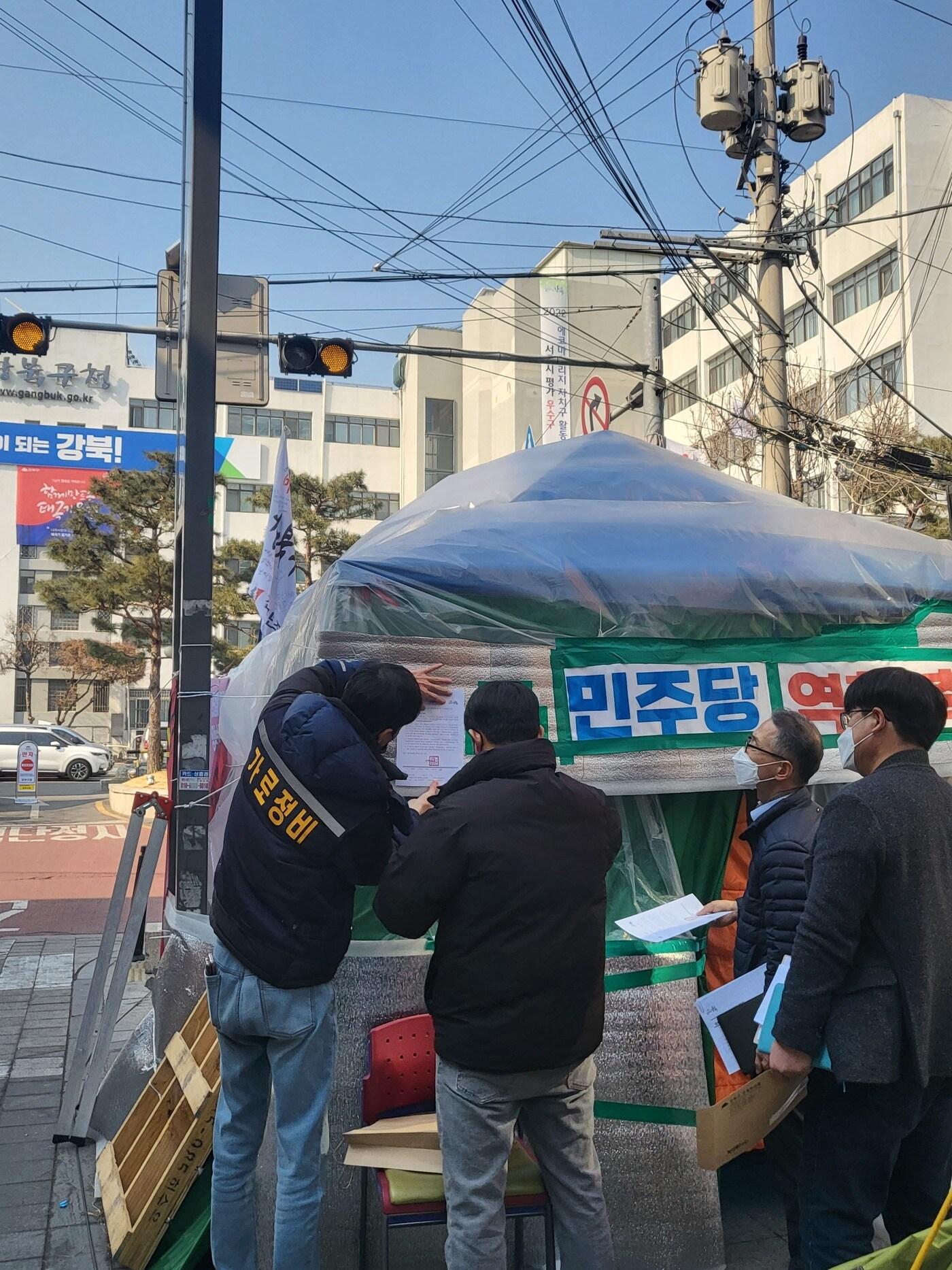 지난 23일 서울 강북구청 관계자들이 구청 앞 도로에 설치된 강북구도시관리공단노조 천막에 계고장을 부착하고 있다. &#40;강북구 제공&#41;