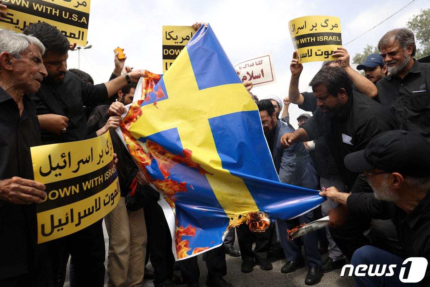이란 시위대가 21일&#40;현지시간&#41; 수도 테헤란에서 최근 스웨덴에서 벌어진 쿠란 소각시위에 항의하는 차원에서 스웨덴 국기에 불을 지르고 있다. 2023.7.21. ⓒ 로이터=뉴스1 ⓒ News1 김성식 기자
