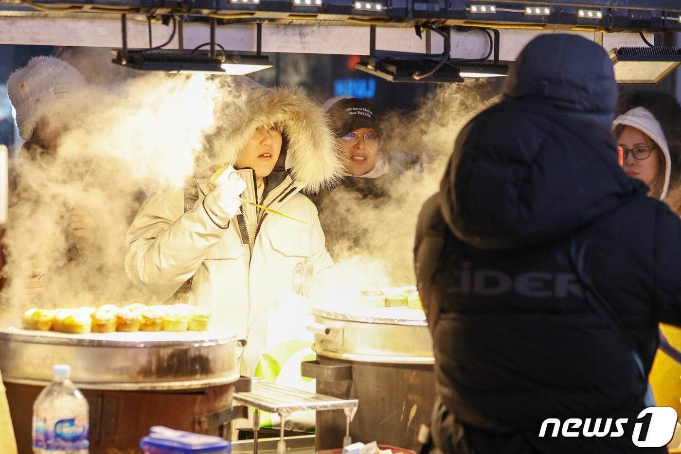 전국에 한파가 몰아닥친 23일 저녁 서울 중구 명동거리의 포장마차에서 외국인 관광객들이 뜨거운 김이 피어오르는 달걀빵을 맛보고 있다. 2024.1.23/뉴스1 ⓒ News1 민경석 기자