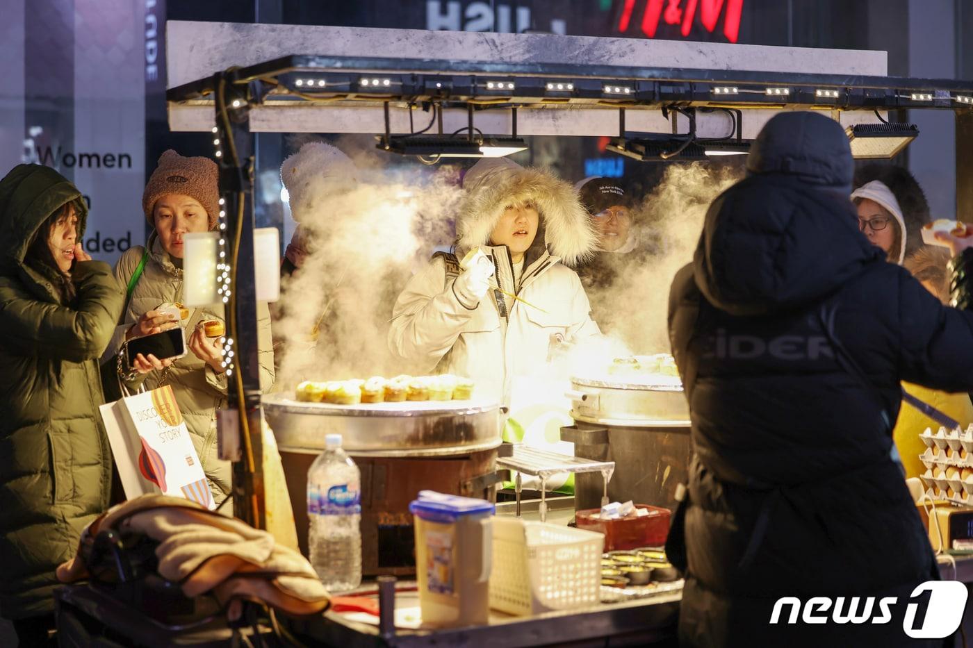 전국에 한파가 몰아닥친 23일 저녁 서울 중구 명동거리의 포장마차에서 외국인 관광객들이 뜨거운 김이 피어오르는 달걀빵을 맛보고 있다. 2024.1.23/뉴스1 ⓒ News1 민경석 기자