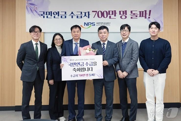 국민연금공단이 주최한 &#39;수급자 700만 명 돌파 기념식&#39;에서 700만 번째 수급자인 박 모 씨&#40;왼쪽에서 세 번째&#41;와 정태규 연금이사&#40;왼쪽에서 네 번째&#41;가 사진 촬영을 하고 있다.&#40;국민연금공단 제공&#41;