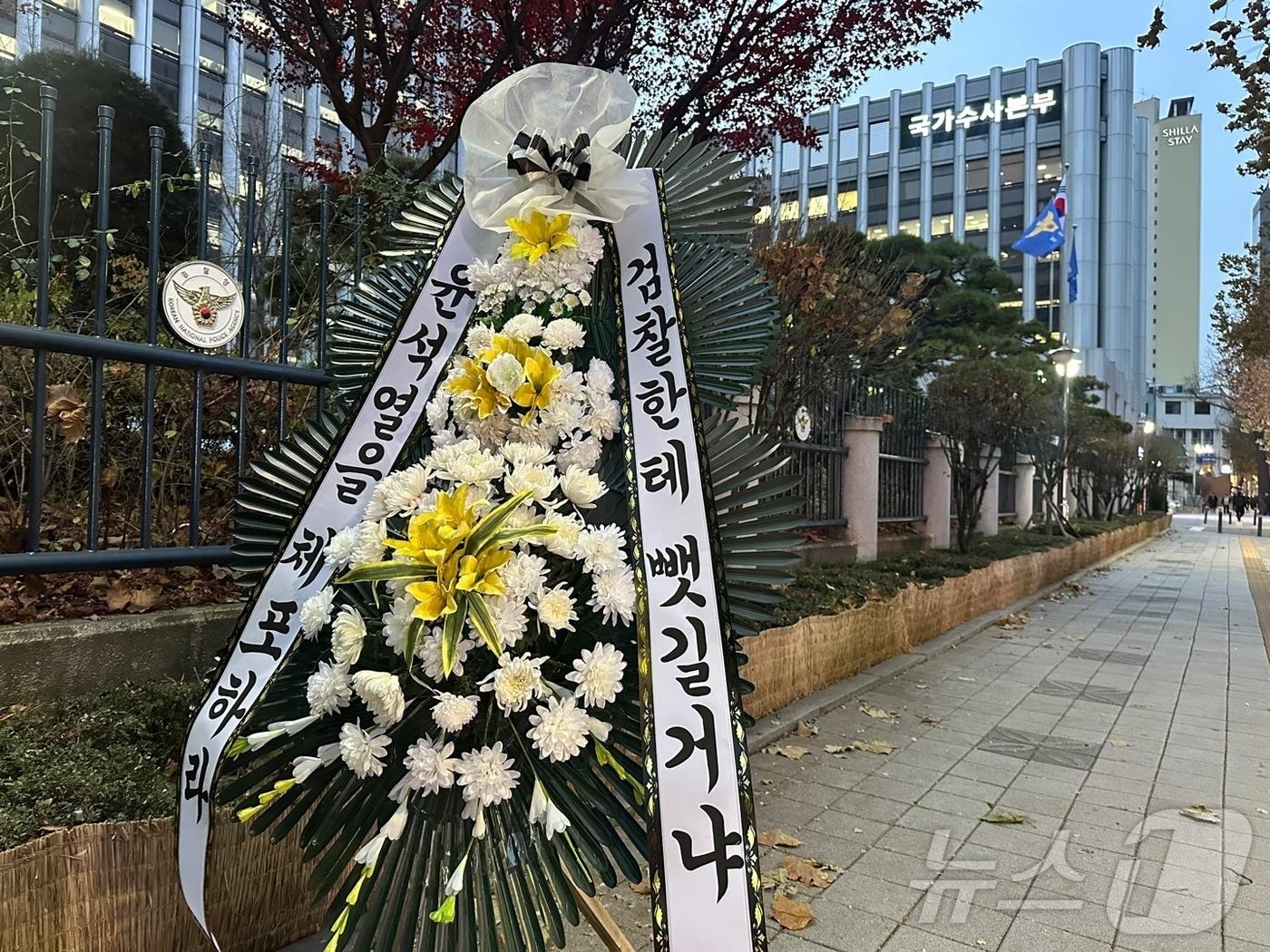 12일 오후 서울 서대문구 미근동 경찰청사 정문 인근 울타리에는 &#34;윤석열을 체포하라, 검찰한테 뺏길거냐&#34; 내용이 담긴 근조화환이 설치됐다.