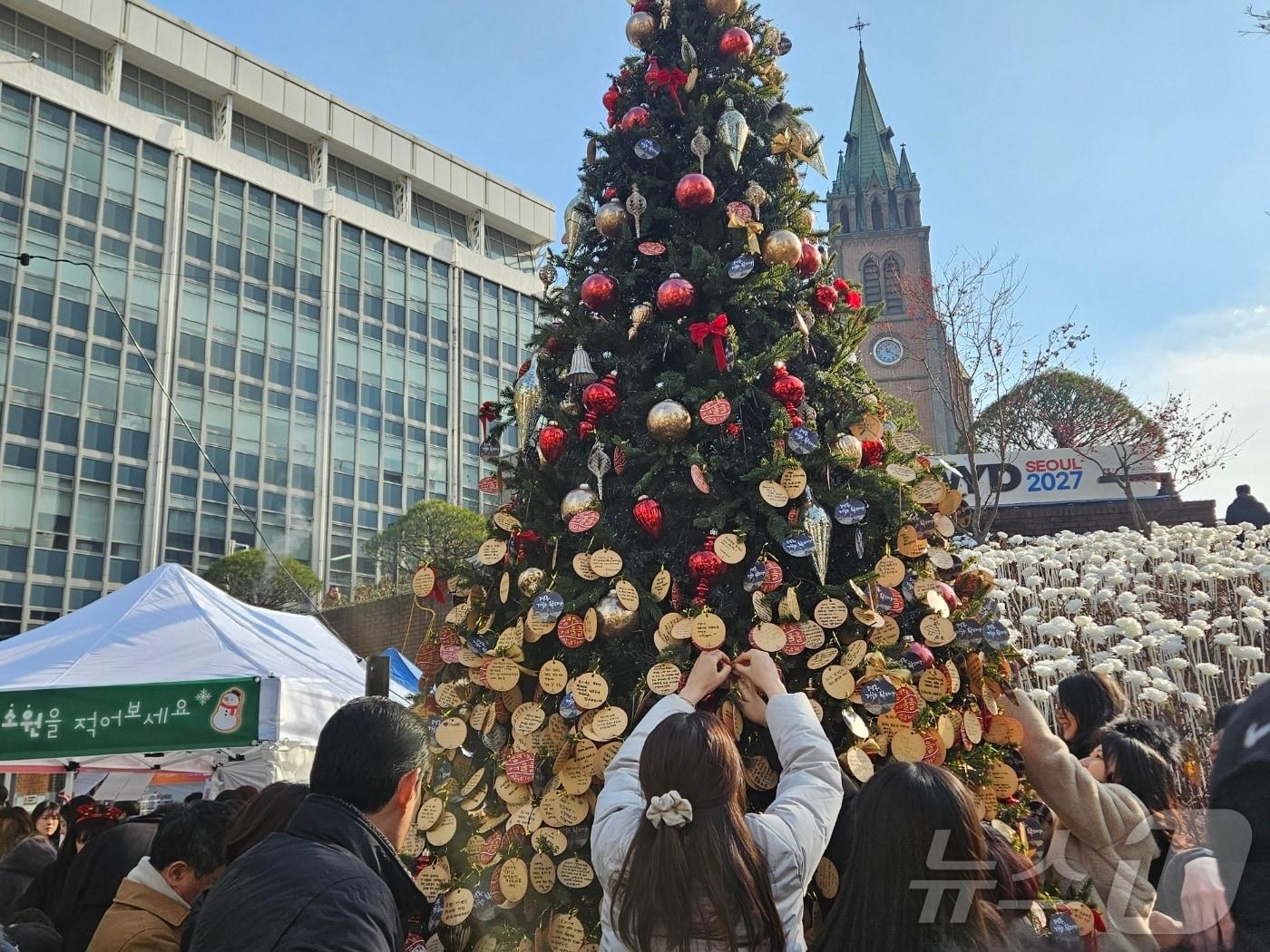 25일 오후 1시쯤 명동성당 앞에서 시민들이 기부를 하고 받은 소원카드에 소원을 적어 크리스마스 트리에 걸고 있다. 2024.12.25/뉴스1 장시온 기자