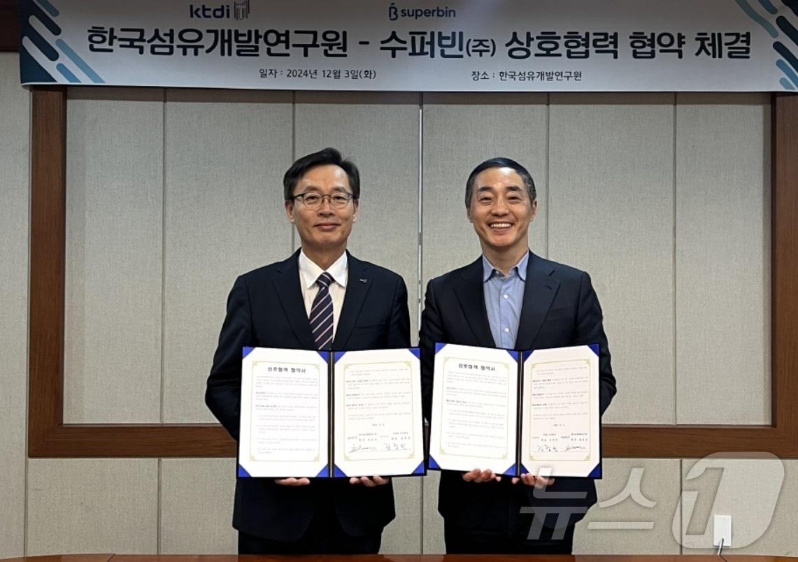 호요승 한국섬유개발연구원장&#40;왼쪽&#41;과 김정빈 수퍼빈㈜ 대표가 상호 협력 협약을 체결한 뒤 협약서를 펼쳐 보이고 있다.&#40;ktdi 제공&#41;