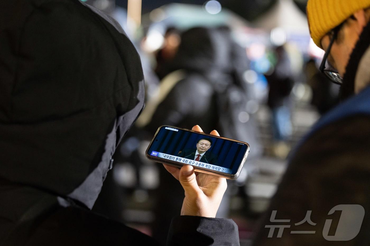 비상계엄 해제 요구 결의안이 국회 본회의에서 통과된 4일 새벽 서울 여의도 국회 인근에서 한 시민이 윤석열 대통령의 비상계엄 해제 관련 담화를 지켜보고 있다. 2024.12.4/뉴스1 ⓒ News1 이재명 기자