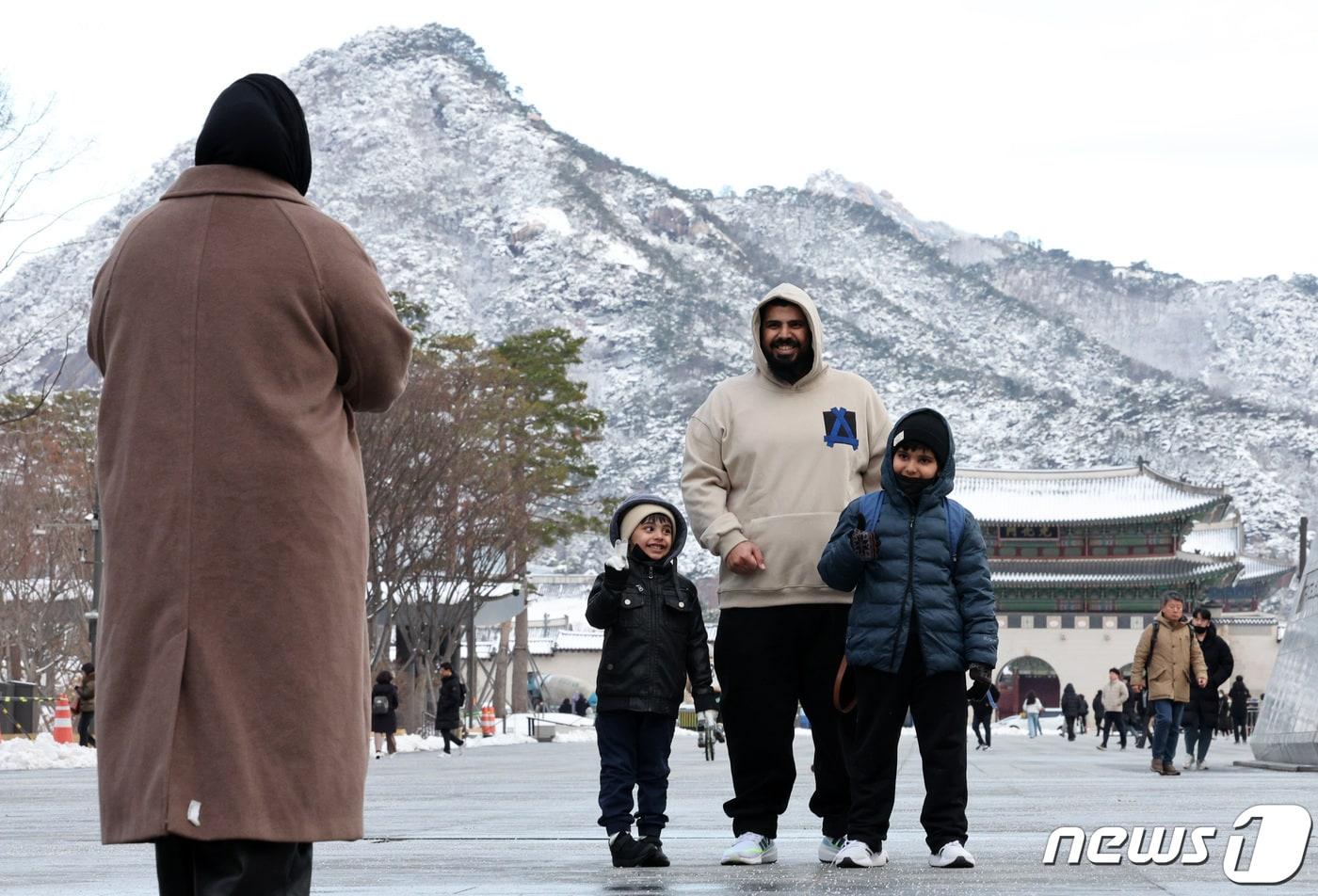 서울 종로구 광화문 네거리에서 두터운 옷을 입은 관광객들이 눈쌓인 북악산을 배경으로 기념촬영하고 있다. 2024.2.23/뉴스1 ⓒ News1 장수영 기자