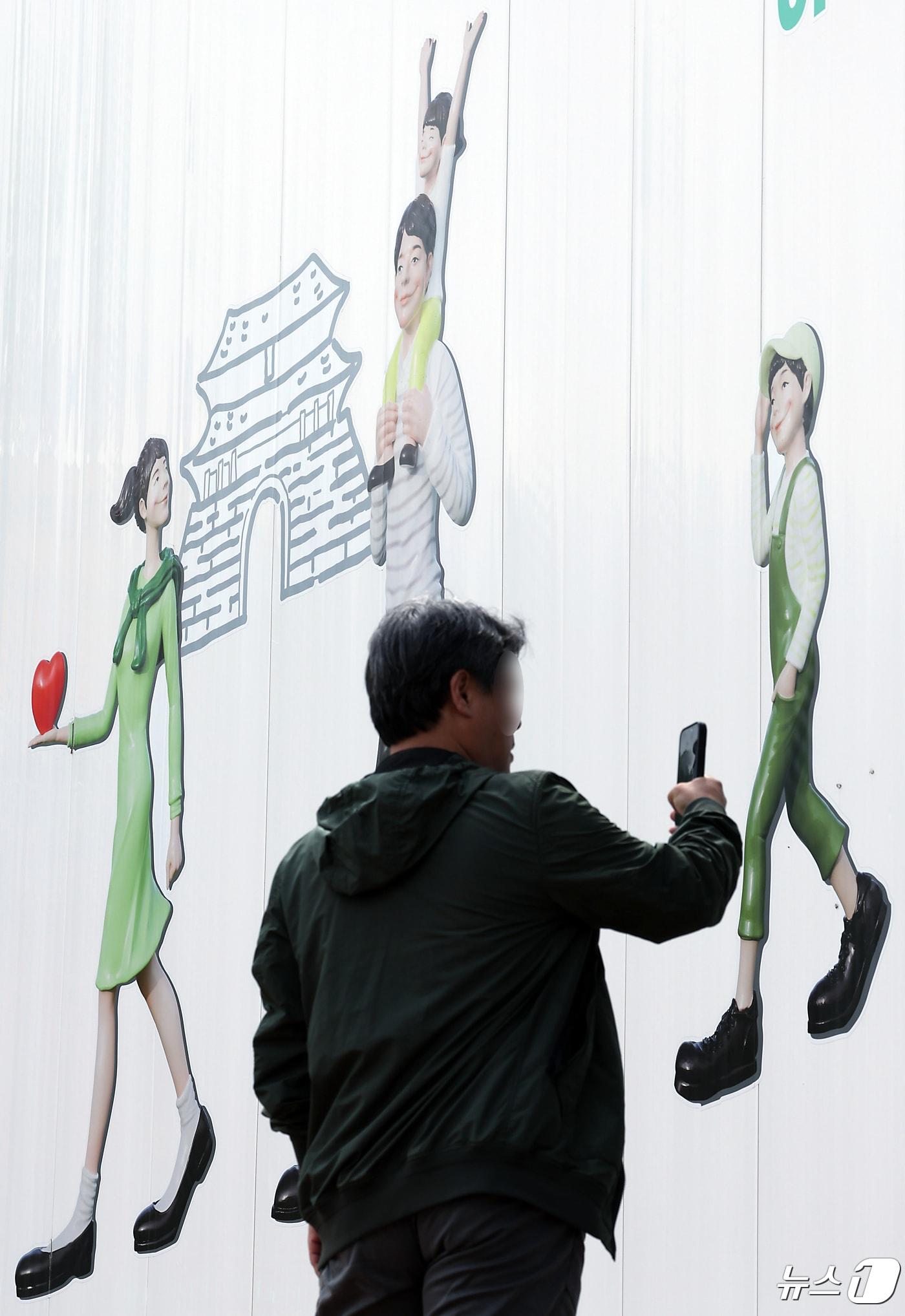  서울 도심의 공사장 가림막에 그려진 행복한 가족 그림 앞으로 시민이 지나고 있다. 2024.4.24/뉴스1 ⓒ News1 박정호 기자