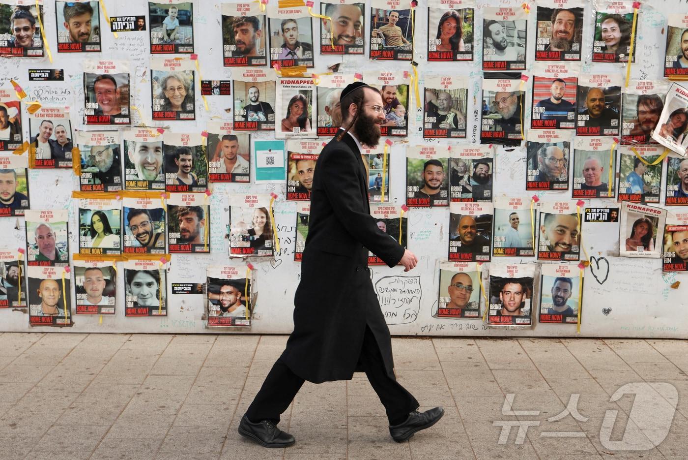 이스라엘 텔아비브의 디젠코프 광장에서 초정토파 유대인 남성이 지난해 10월7일 하마스에 의해 납치된 인질들의 석방을 기원하는 포스터 앞을 지나고 있다. 2024.05.21. ⓒ 로이터=뉴스1 ⓒ News1 정윤영 기자