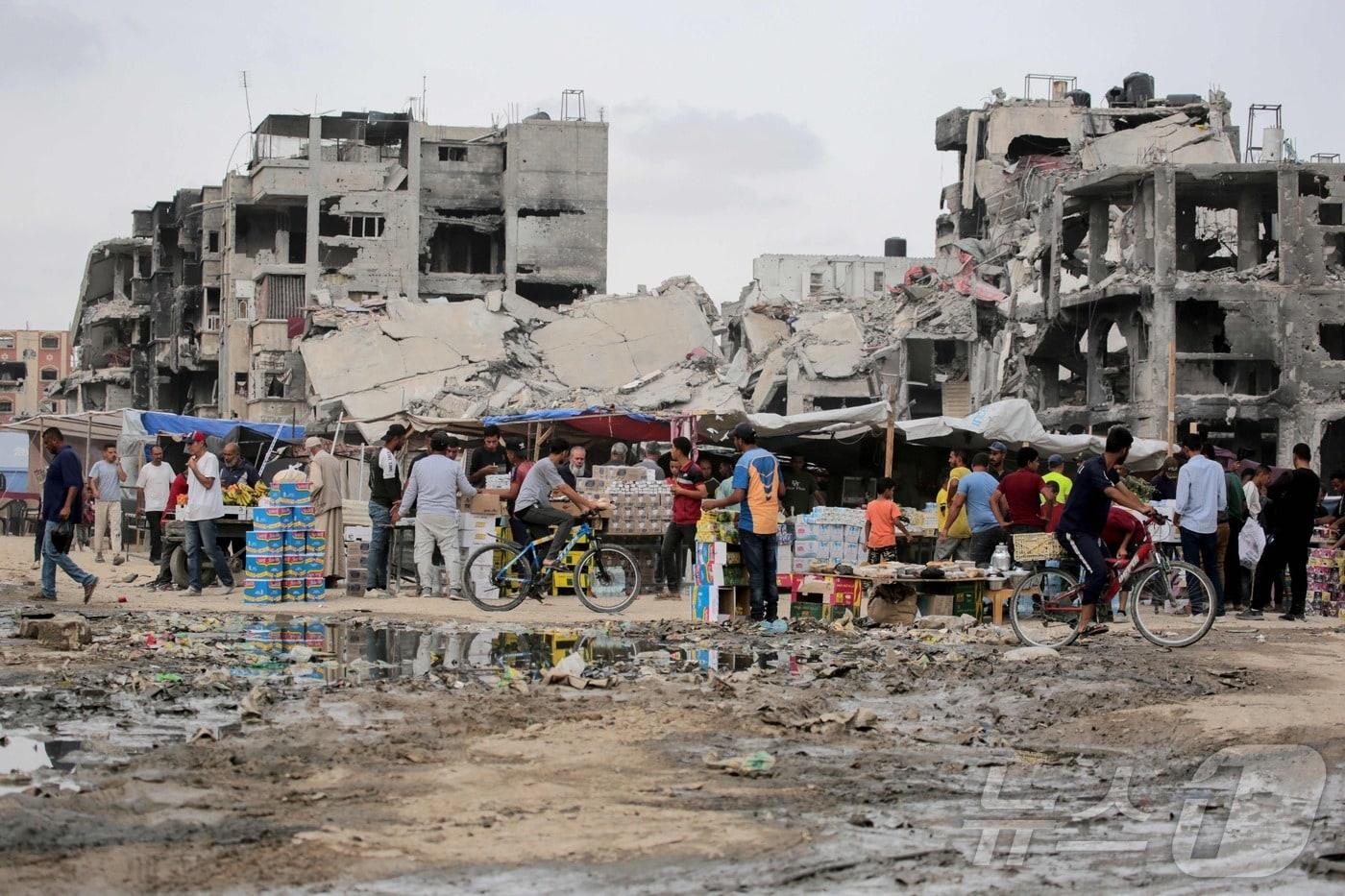 28일&#40;현지시간&#41; 가자지구 남부 칸 유니스에서 팔레스타인인들이 이스라엘의 공습으로 무너진 건물을 배경으로 생필품을 구하고 있다. 2024.05.28/ ⓒ AFP=뉴스1 ⓒ News1 권진영 기자
