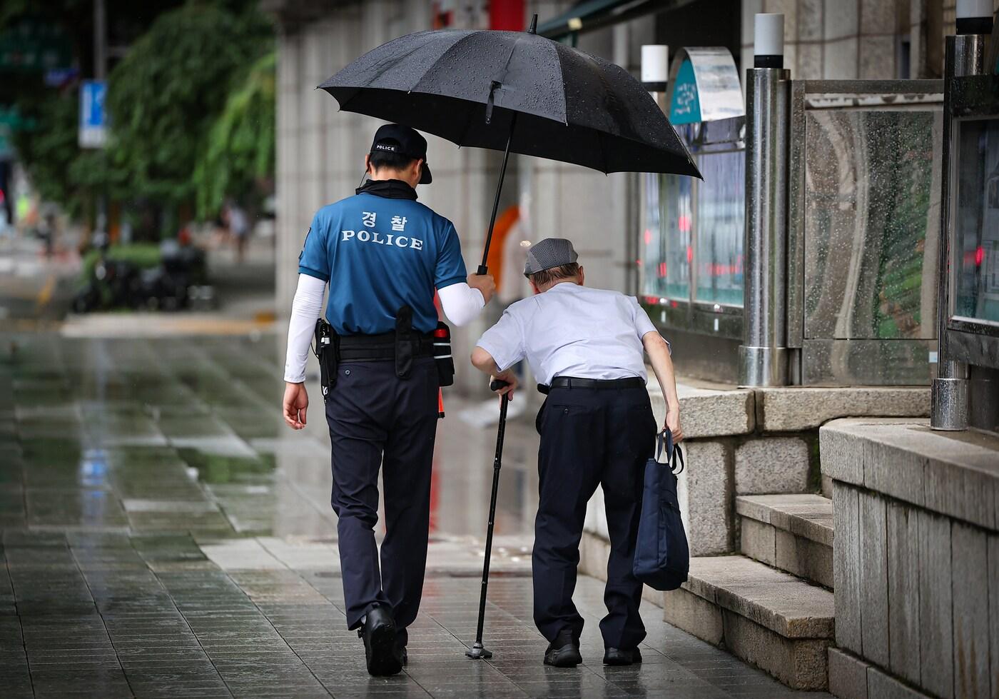 7일 오전 비가 내리는 서울 종로구 광화문역 인근에서 경찰관이 한 어르신에게 우산을 씌어주고 있다. 2024.8.7/뉴스1 ⓒ News1 김진환 기자